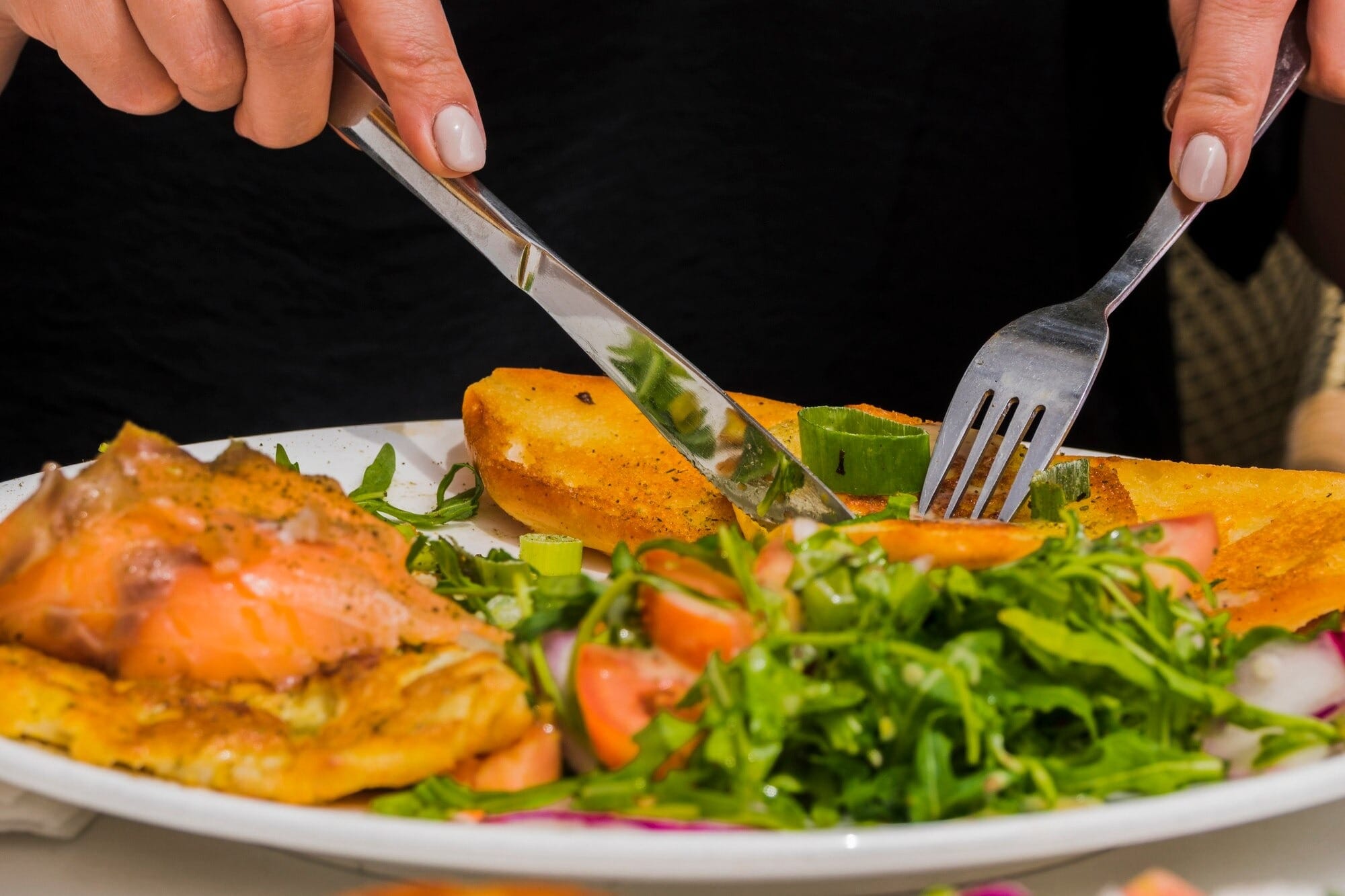 Prato de almoço nutritivo e rápido com salmão temperado, batatas douradas e salada colorida sendo degustado com garfo e faca
