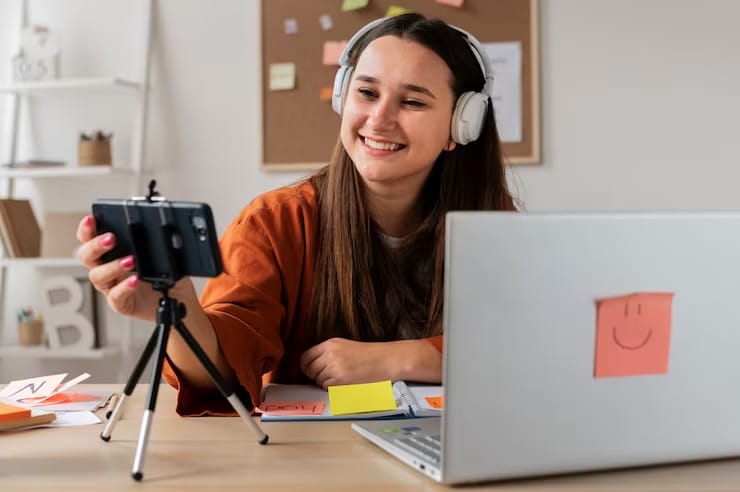 Jovem estudante sorridente assistindo canais do YouTube para aprender com fones de ouvido e smartphone em tripé