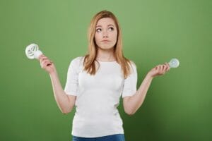 Mulher pensativa comparando lâmpada fluorescente compacta e lâmpada LED incandescente, ilustrando a escolha entre diferentes tipos de iluminação para casa