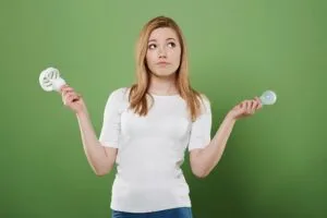 Mulher pensativa comparando lâmpada fluorescente compacta e lâmpada LED incandescente, ilustrando a escolha entre diferentes tipos de iluminação para casa