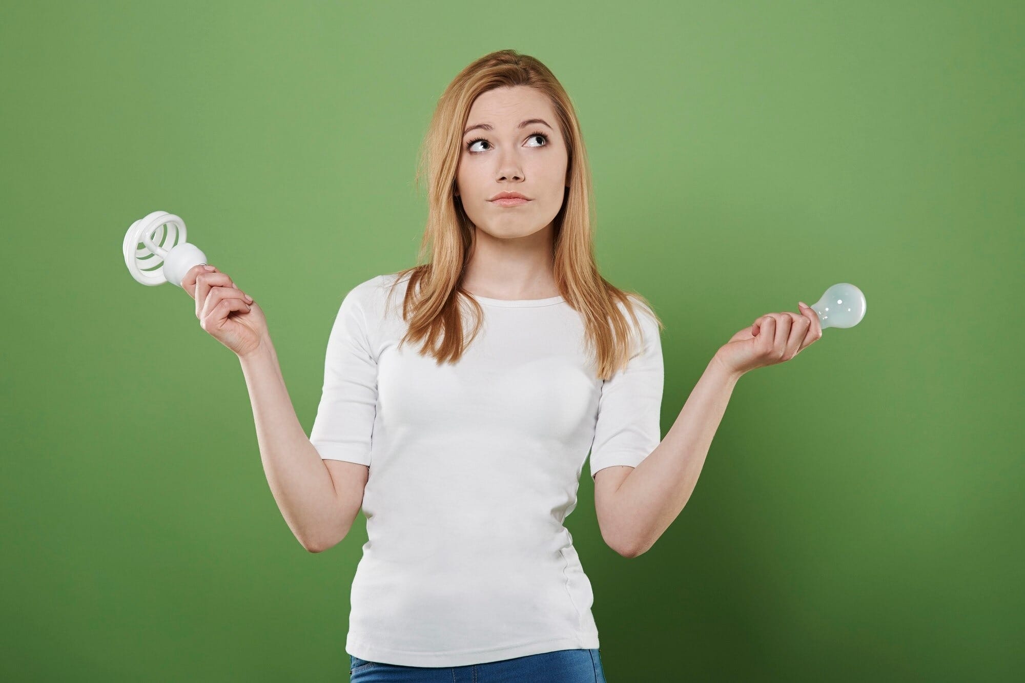 Mulher pensativa comparando lâmpada fluorescente compacta e lâmpada LED incandescente, ilustrando a escolha entre diferentes tipos de iluminação para casa