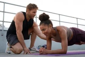 Casal praticando crossfit em casa com exercícios de prancha e peso corporal em ambiente doméstico iluminado