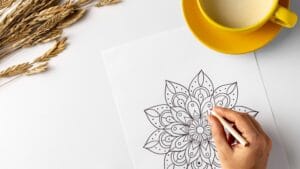 Mão feminina colorindo desenho de mandala para adultos com xícara de café amarela e decoração minimalista