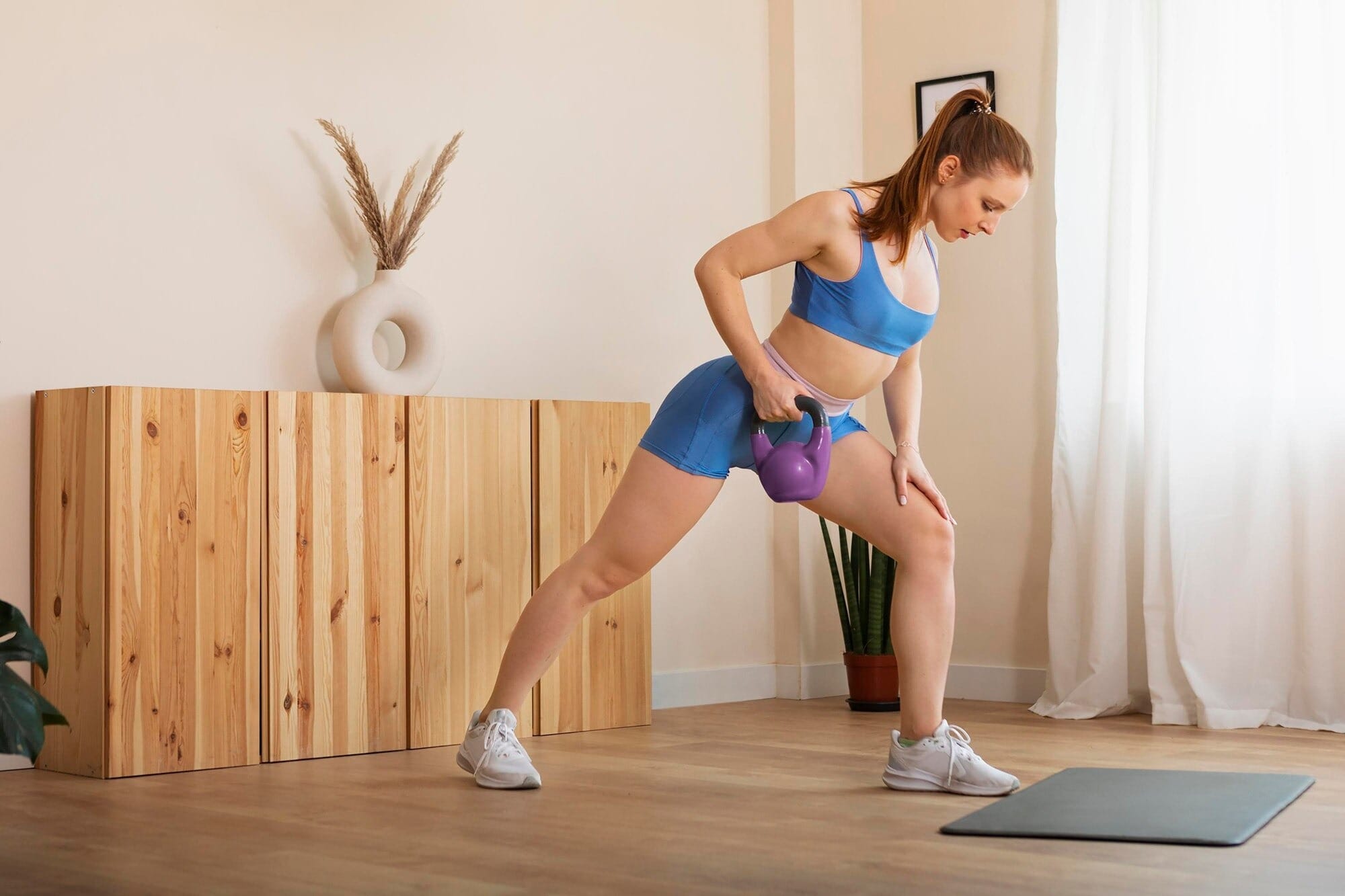 Mulher praticando exercícios para perder culote em casa com kettlebell, fazendo afundo lateral para tonificar e afinar as coxas