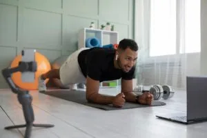Iniciante praticando exercício de prancha em casa seguindo vídeo de treino no laptop com equipamentos simples