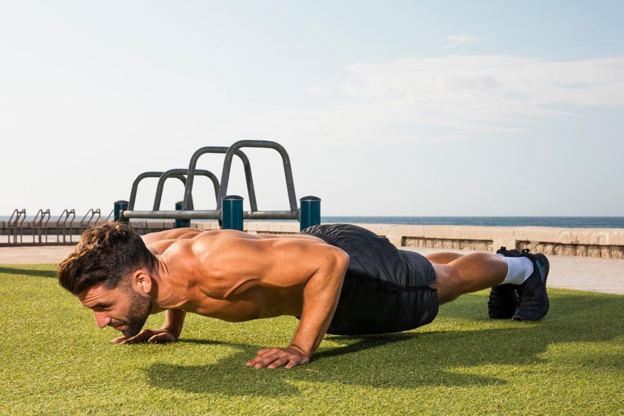 Homem fazendo prancha em treino de abdômen ao ar livre na praia, demonstrando exercício funcional para core