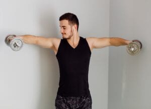 Homem realizando exercício de elevação lateral com halteres para treinar tríceps definido e eliminar flacidez nos braços