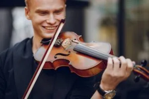Jovem sorridente tocando violino para iniciantes com arco na posição correta, demonstrando a postura básica do instrumento